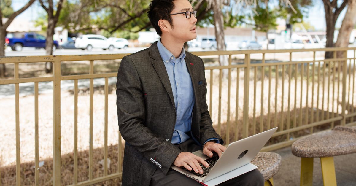 Homme d'affaires en tenue décontractée utilisant un ordinateur portable en extérieur, adoptant un mode de vie de travail à distance.