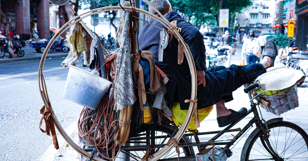 Un homme assis sur un vélo fortement chargé dans les rues animées de la ville, capturant la vie urbaine.
