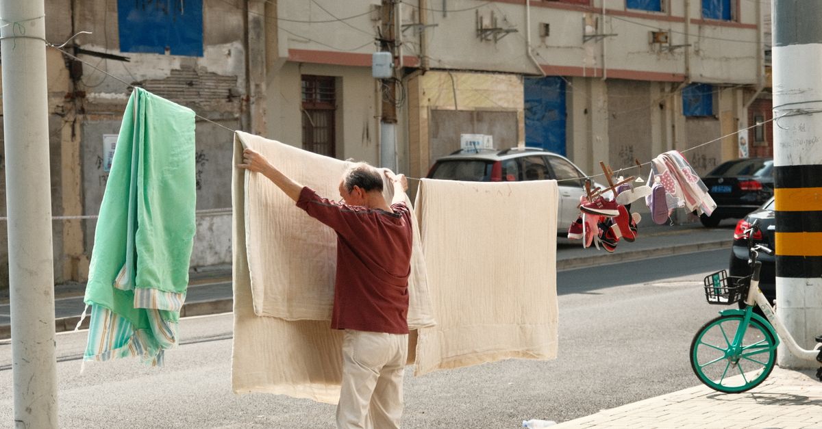 Un homme accroche du linge dans une rue de Shanghai, capturant la vie quotidienne et la culture urbaine.