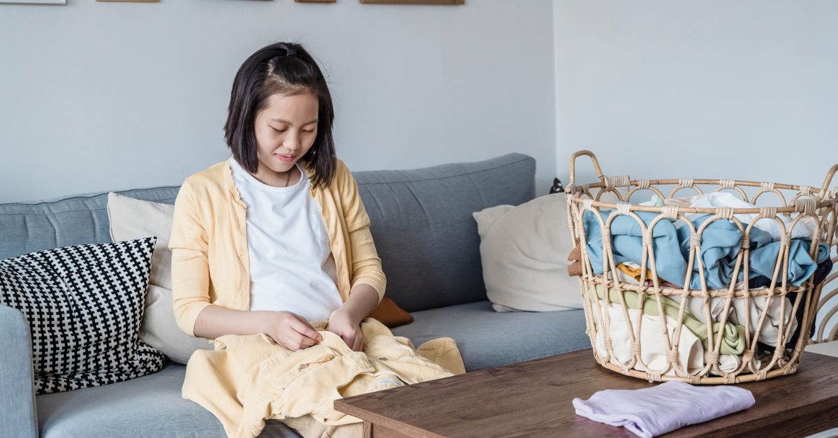Fille asiatique pliant des vêtements sur un canapé à la maison, montrant les tâches ménagères.