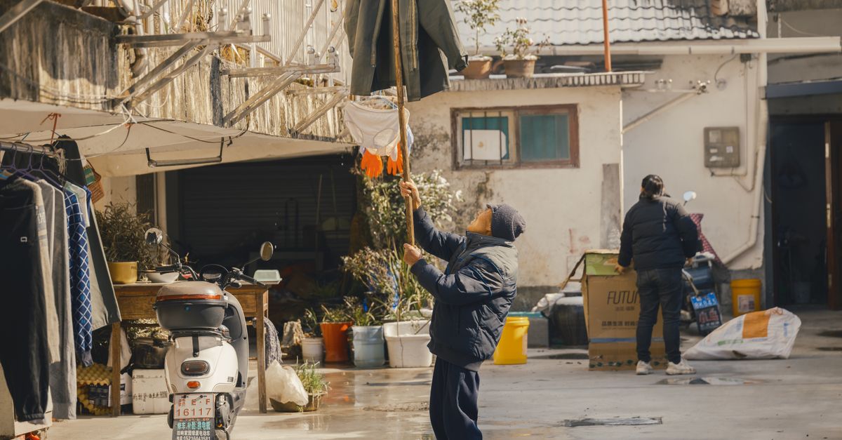 Un homme âgé suspend du linge à l'extérieur dans un cadre urbain, offrant un aperçu de la vie quotidienne.