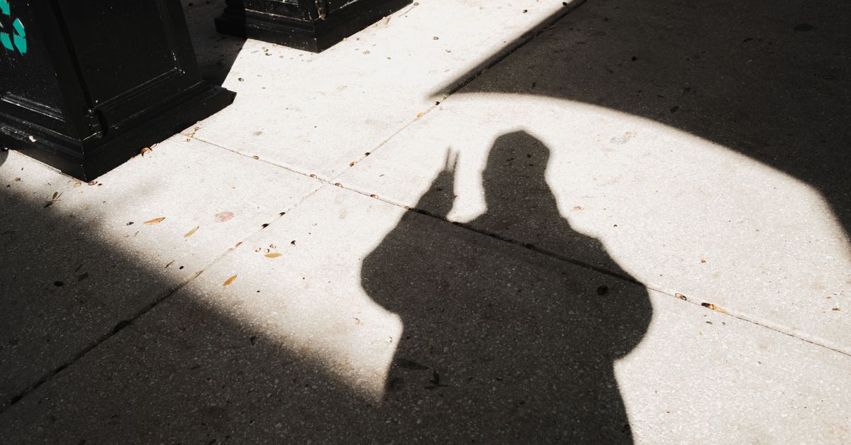Une silhouette d'ombre faisant un signe de paix sur un trottoir urbain ensoleillé.