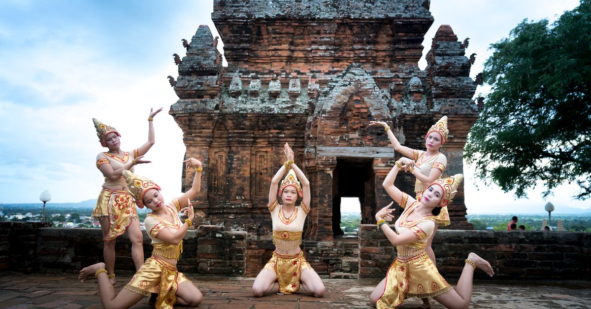 Des danseuses traditionnelles en costumes dorés se produisent dans un ancien temple, mettant en valeur le patrimoine culturel.