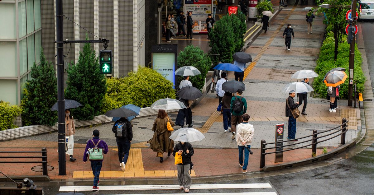 Des personnes traversent une rue de Tokyo avec des parapluies par temps de pluie, illustrant la vie urbaine.