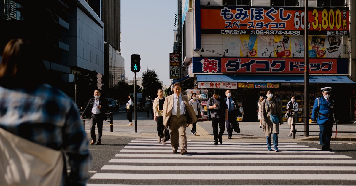 Un carrefour animé dans une ville japonaise avec des piétons divers traversant un passage piéton.
