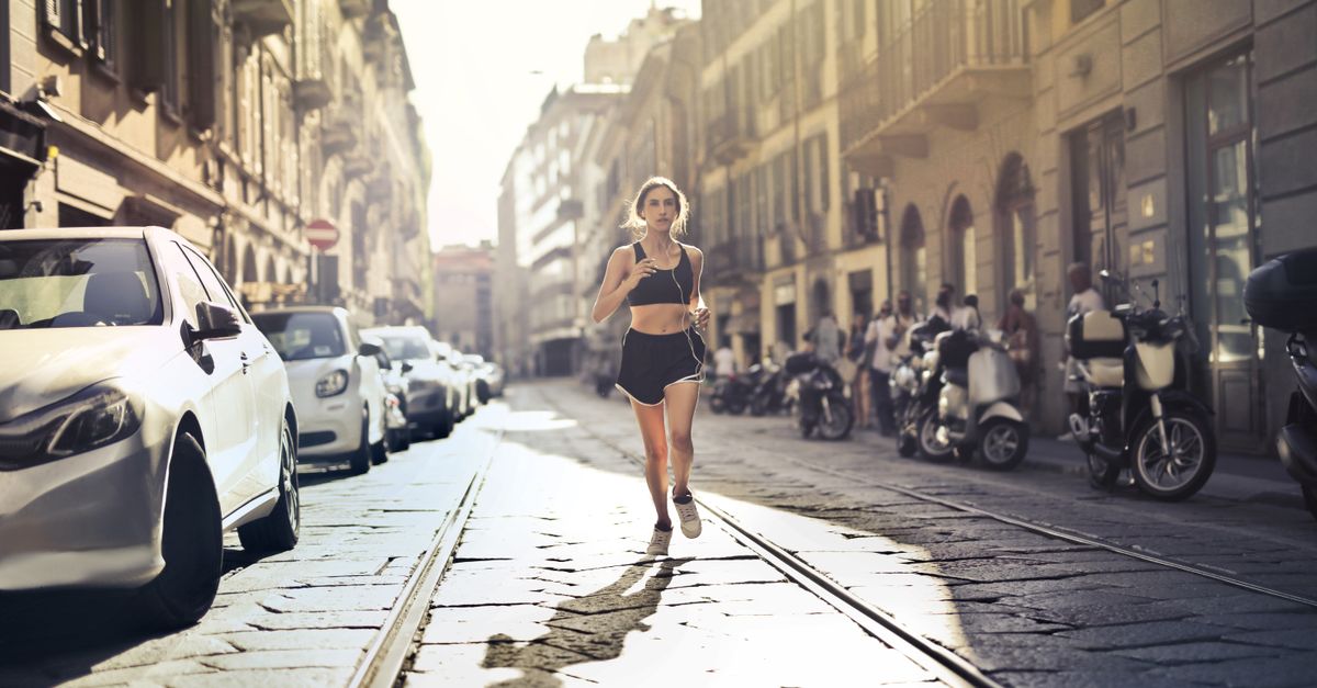 Femme joggeuse énergique courant dans une rue de la ville en tenue de sport par une journée ensoleillée.