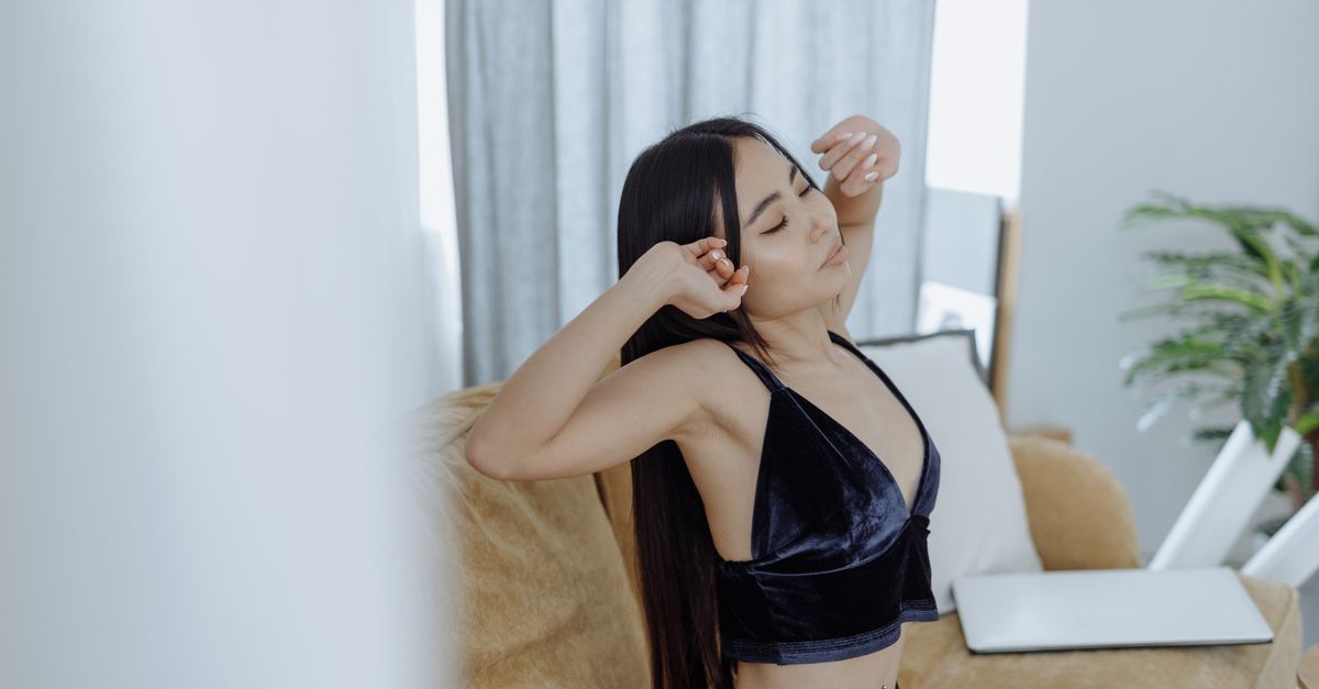 Femme aux cheveux longs s'étire à l'intérieur, adoptant une routine matinale calme. Parfait pour des thèmes de mode de vie et de bien-être.