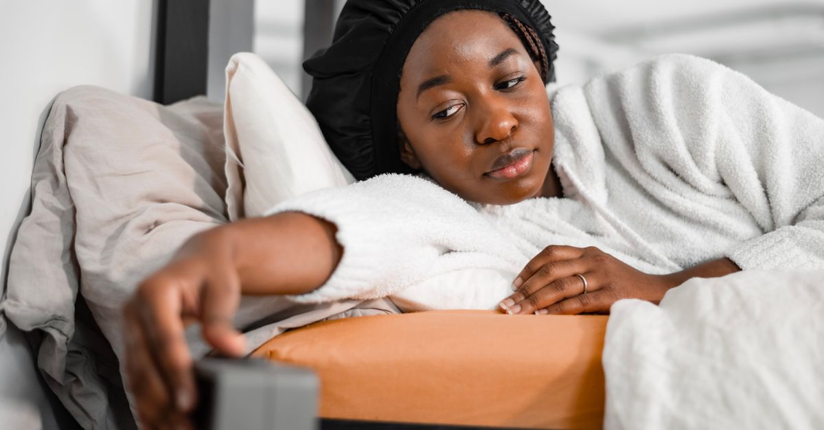 Femme dans un peignoir douillet atteignant le réveil dans la chambre, se réveillant rafraîchie.