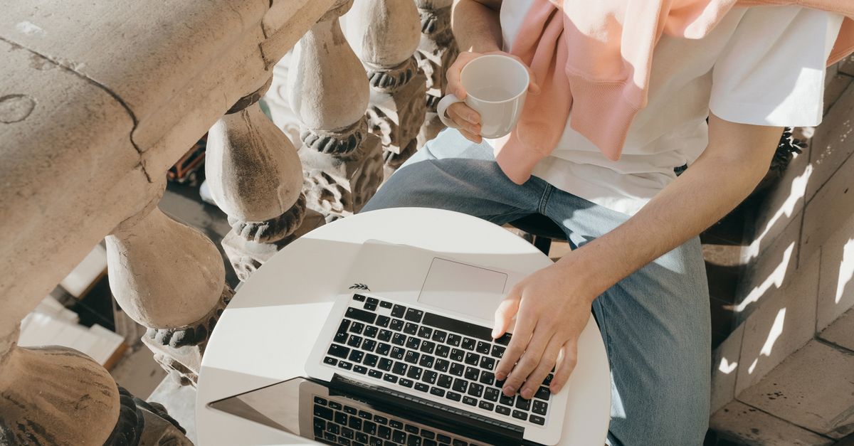 Personne travaillant sur un ordinateur portable avec un café sur un balcon ensoleillé.