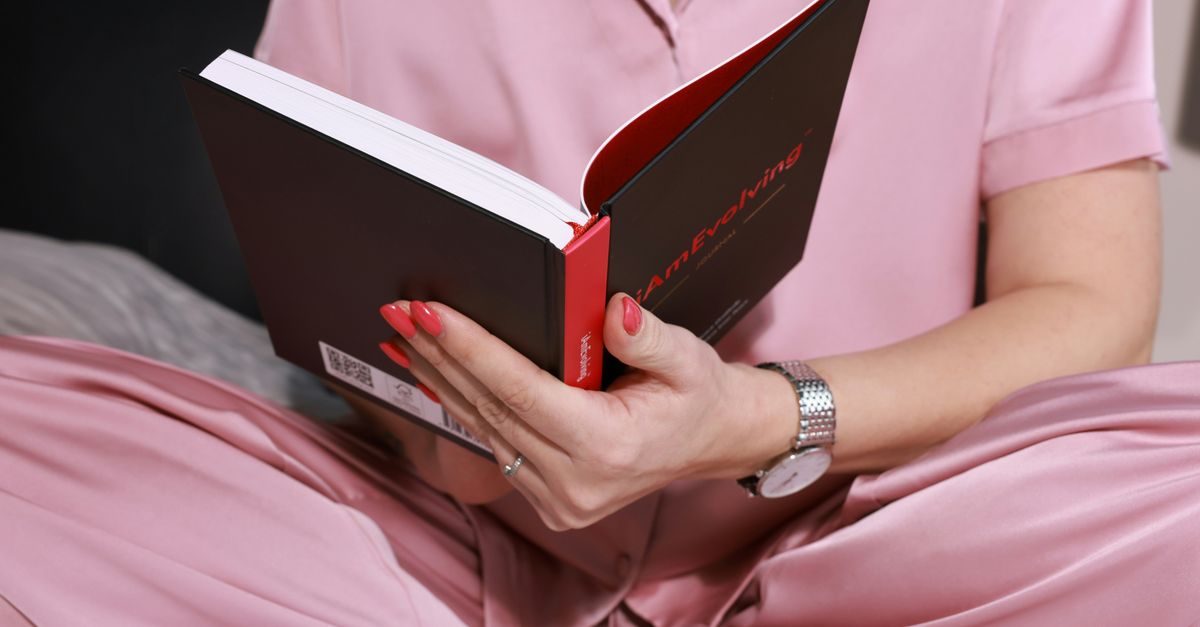 Une femme vêtue d'un pyjama en soie rose lit un journal, se concentrant sur la pleine conscience et la relaxation.