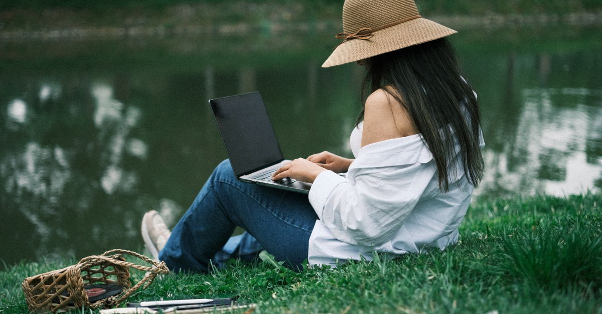 Jeune femme utilisant un ordinateur portable dans un parc au bord d'un lac, profitant du télétravail en pleine nature.
